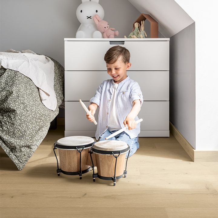 barn spiller på trommer i et soveværelse med beige vinylgulv